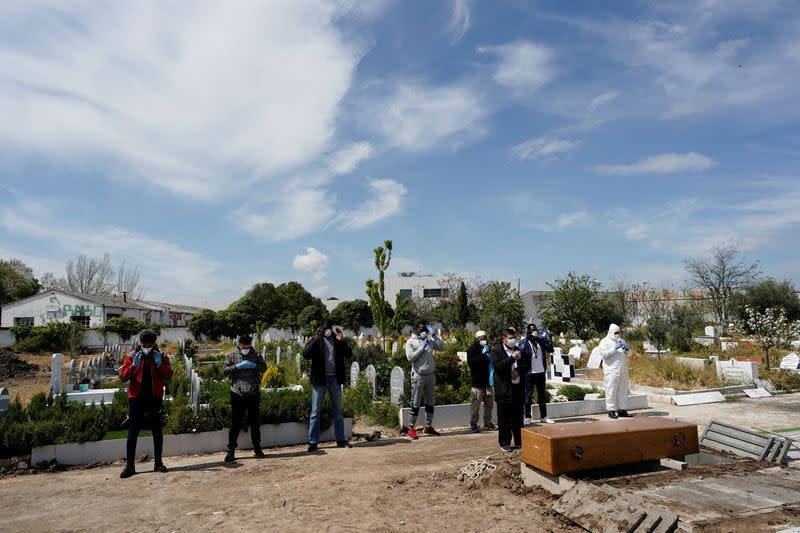 People wearing protective face masks pray in front of the coffin of a person who died of coronavirus disease (COVID-19), at the Spanish muslim military cemetery, in Grinon