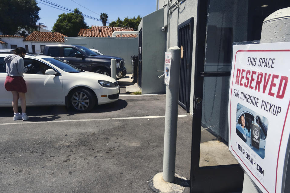 In this Thursday, April 16, 2020, photo, wearing a protective mask and gloves, budtender Alexi Ezdrin serves a customer with curbside assistance at The Higher Path cannabis dispensary in the Sherman Oaks section of Los Angeles. Monday is April 20, or 4/20. That’s the code for marijuana’s high holiday, which is usually marked with outdoor festivals and communal smoking sessions. But this year, stay-at-home orders have moved the party online as the marijuana market braces for an economic blow from the coronavirus crisis. (AP Photo/Richard Vogel)