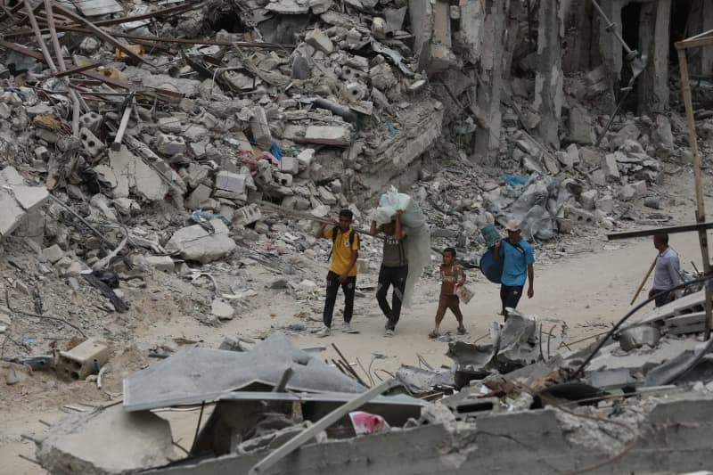 People walk between damaged buildings and streets as debris removal and cleaning works continue after the withdrawal of Israel from Khan Yunis. Palestinians started returning to the city and trying to live their lives despite the heavily damaged infrastructure system. Omar Ashtawy/APA Images via ZUMA Press Wire/dpa