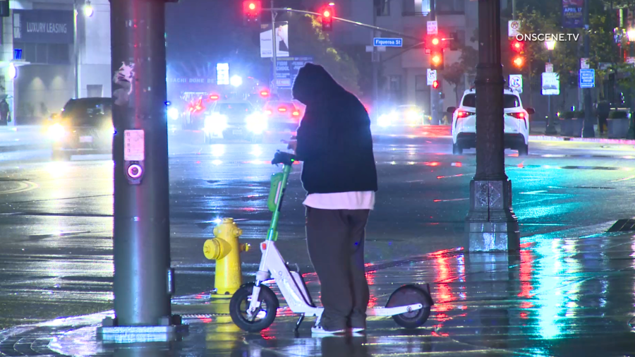 A man stands near a scooter as it rains in downtown Los Angeles on March 30, 2024.