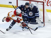 Calgary Flames' A.J. Greer (18) attempts a backhand shot on Winnipeg Jets goaltender Connor Hellebuyck (37) as Josh Morrissey (44) defends during the third period of an NHL hockey game Thursday, April 4, 2024, in Winnipeg, Manitoba. (John Woods/The Canadian Press via AP)