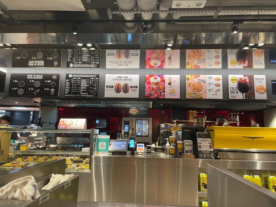 Metallic, warehouse-style counter with cash registers and a black, red, and white menu with McDonald's items overhead