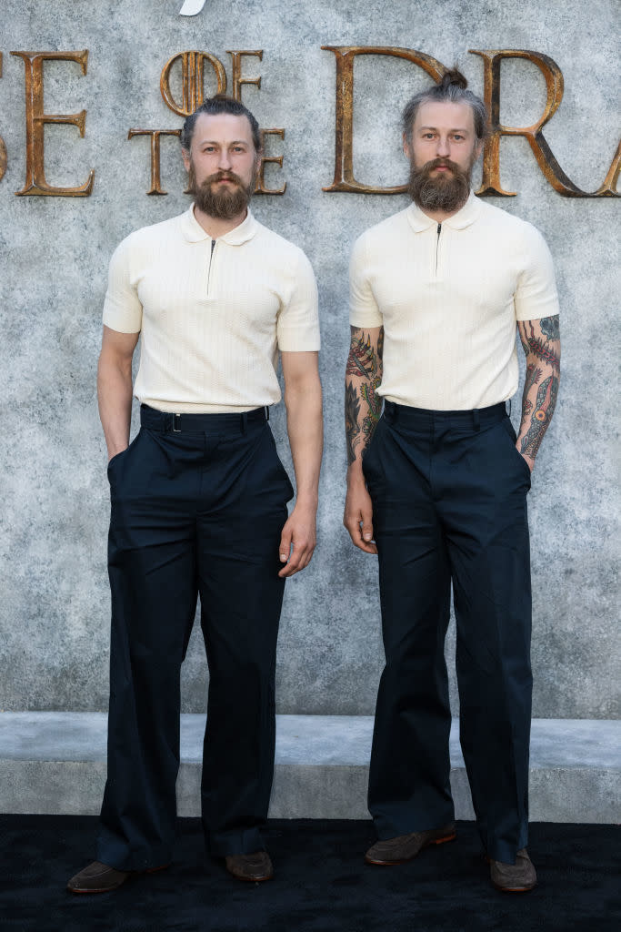 Two men with beards and similar hairstyles wear white short-sleeve collared shirts and dark trousers at a "House of the Dragon" event