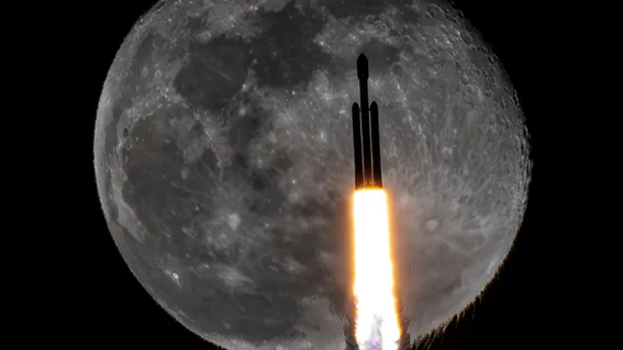  A silhouetted triple booster rocket passes in front of a full moon as fire spews from its engines. 