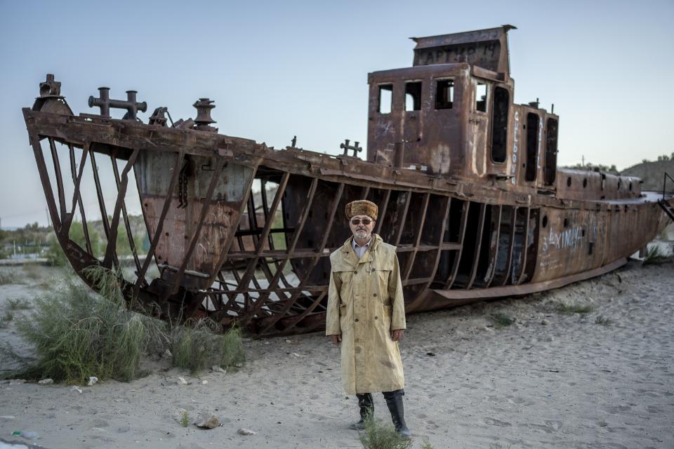 Kolgay poses for a photo in front of an old boat in the area where the Aral Sea once was in Muynak, Uzbekistan, Thursday, July 13, 2023. (AP Photo/Ebrahim Noroozi)