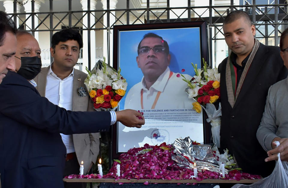 Businessmen pose to put candles and rose petals next to the portrait of a Sri Lankan manager of a sports equipment factory, as they pay tribute to him outside the office of Sialkot Chamber of Commerce and Industry in Sialkot, Pakistan, Saturday, Dec. 4, 2021. Police arrested multiple suspects and detained dozens of others in the lynching of the Sri Lankan employee at the sports equipment factory in eastern Pakistan, officials said Saturday. (AP Photo/Shahid Ikram)