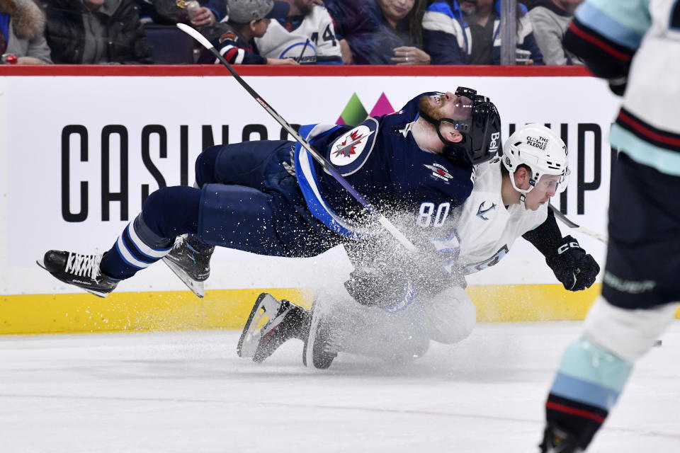 Seattle Kraken's Eeli Tolvanen (20) dumps Winnipeg Jets' Pierre-Luc Dubois (80) during the second period of an NHL game in Winnipeg, Manitoba on Tuesday Feb. 14, 2023. (Fred Greenslade/The Canadian Press via AP)