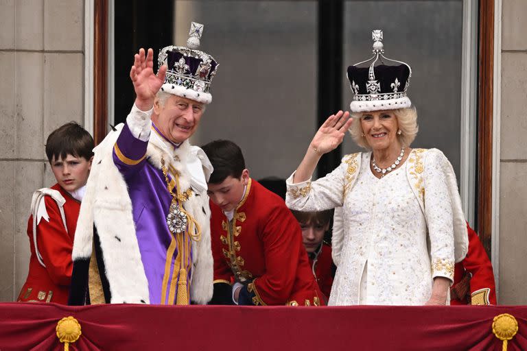 El Rey Carlos III de Gran Bretaña, con la Corona Imperial de Estado, y la Reina Camilla, con una versión modificada de la Corona de la Reina María, saludan desde el balcón del Palacio de Buckingham tras ver el sobrevuelo de la Royal Air Force en el centro de Londres el 6 de mayo de 2023, después de sus coronaciones.  (Foto de Oli SCARFF / AFP)
