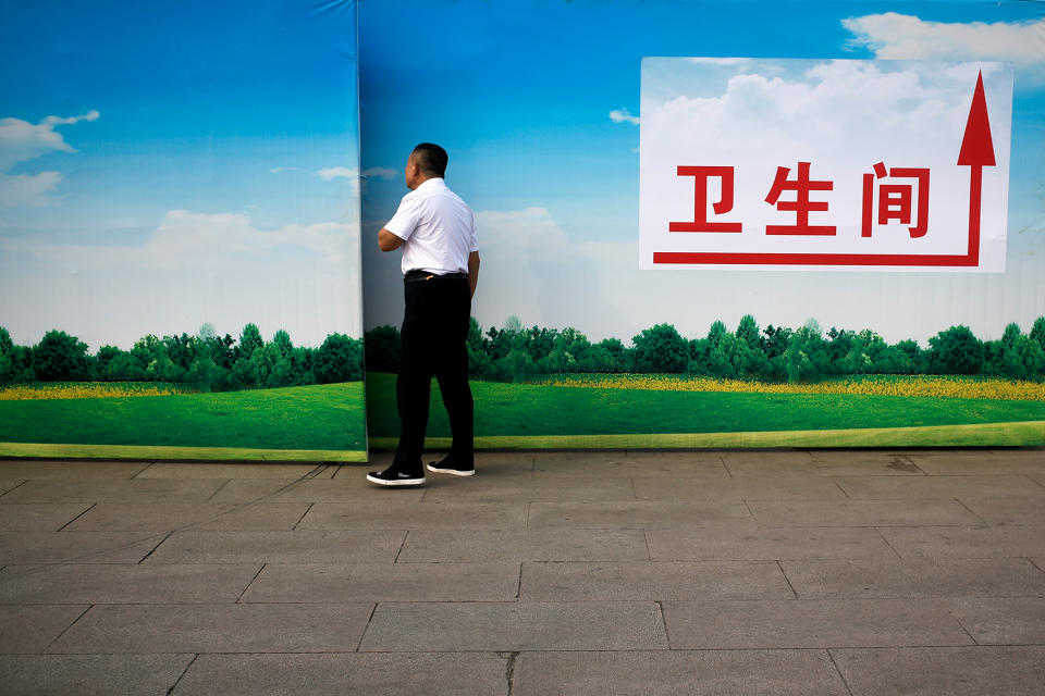 <p>A man peeps into scenery boards used to fence off a construction site near Tiananmen Gate in Beijing. The direction words on the board reads: “Toilet” (AP Photo/Andy Wong) </p>