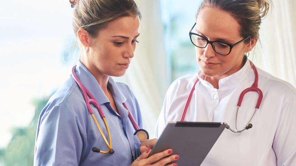 Young brazilian doctor and nurse checking patient information on a tablet device.