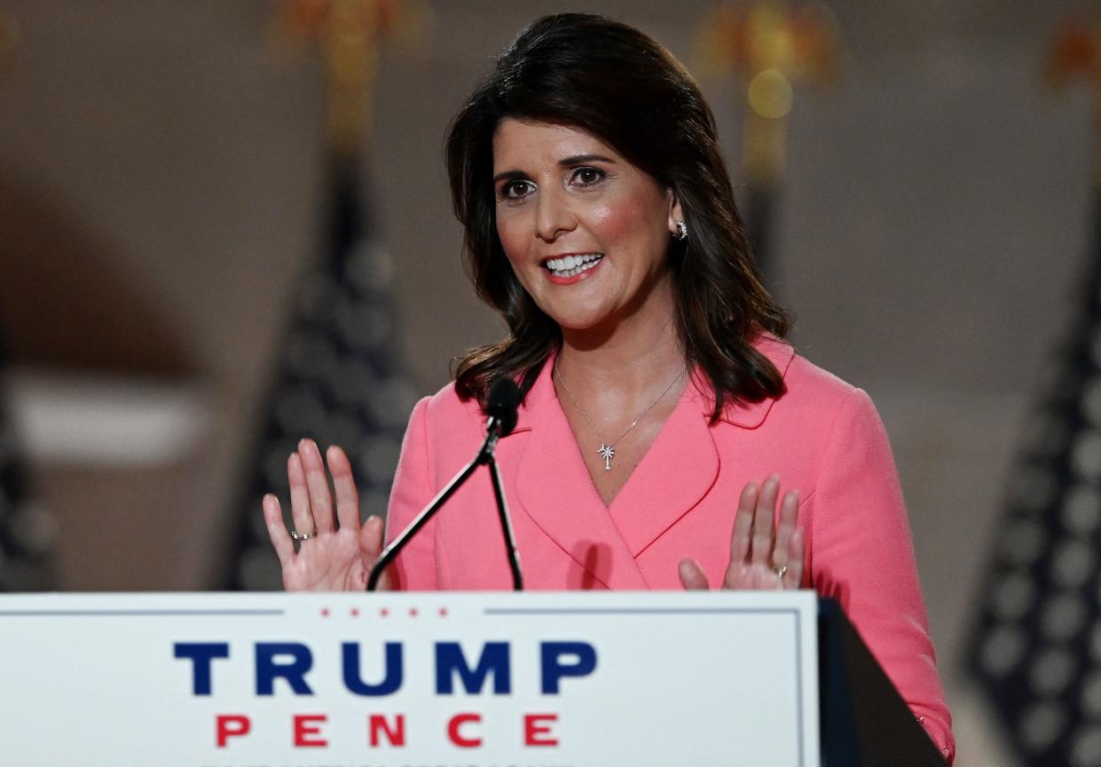 Nikki Haley, in pink suit, at a podium labeled Trump Pence.