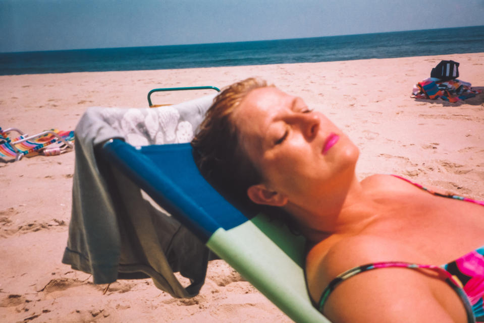 A woman in floral swimwear relaxes on a beach chair, eyes closed, enjoying the sun by the sea