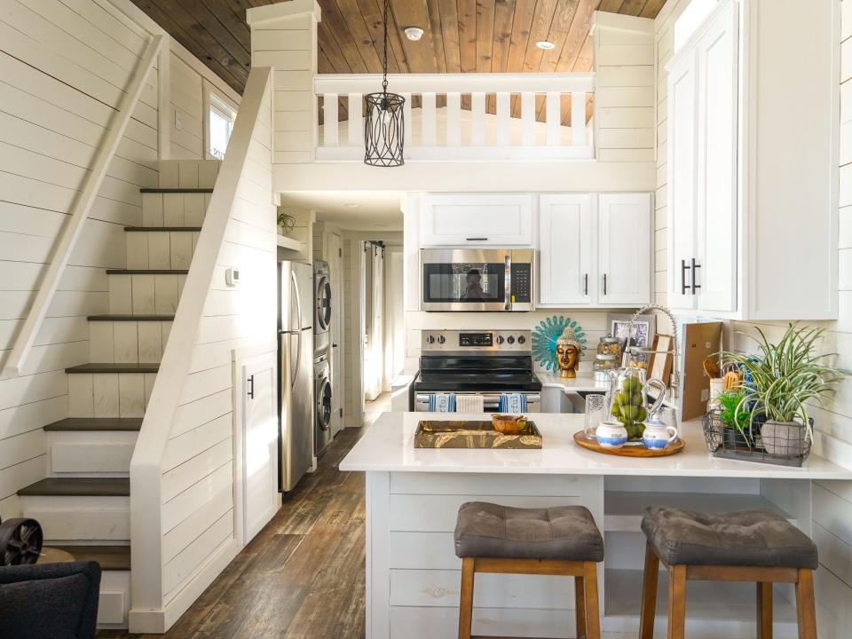 Inside a tiny home with stairs on the left leading up to a loft and a kitchen on the right