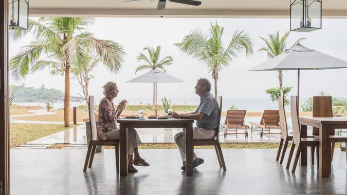 Two people sitting face to face enjoying dinner with view of swimming pool and terrace through open plan room.