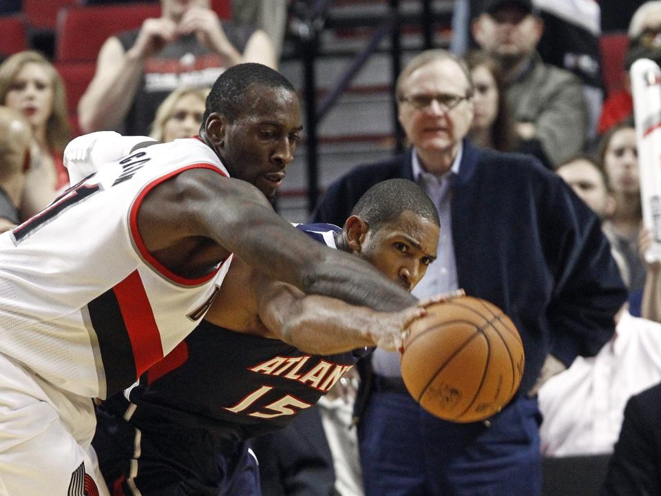 Two basketball players reach for a basketball as Paul Allen looks on in the background