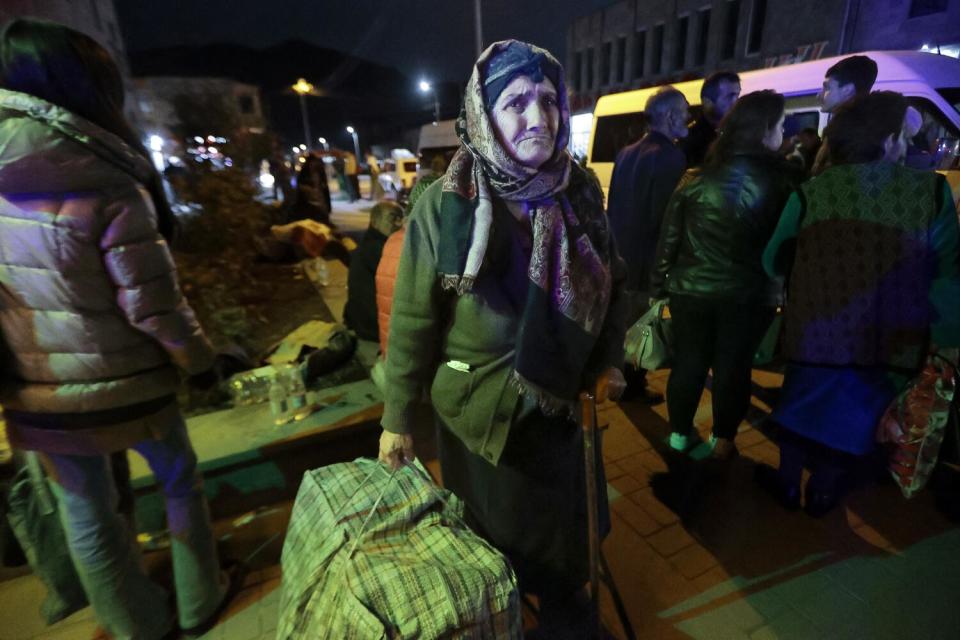 A standing woman holds a big bag, with other people standing near her.