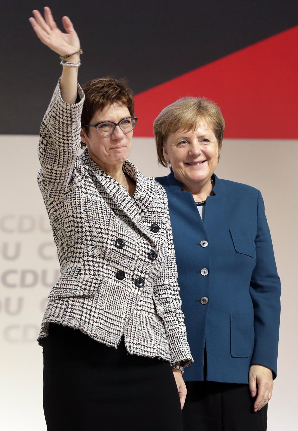 Newly elected CDU chairwoman Annegret Kramp-Karrenbauer, left, is flanked by German Chancellor Angela Merkel, right, as she waves during the party convention of the Christian Democratic Party CDU in Hamburg, Germany, Friday, Dec. 7, 2018, after German Chancellor Angela Merkel didn't run again for party chairmanship after more than 18 years at the helm of the party. (AP Photo/Michael Sohn)