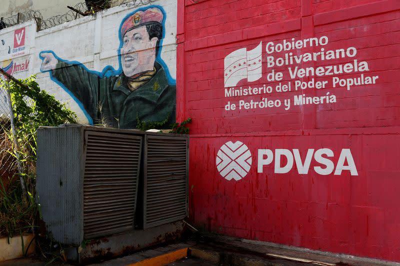 FILE PHOTO: The logo of the Venezuelan state oil company PDVSA is seen next to a mural depicting Venezuela's late President Hugo Chavez at a gas station in Caracas