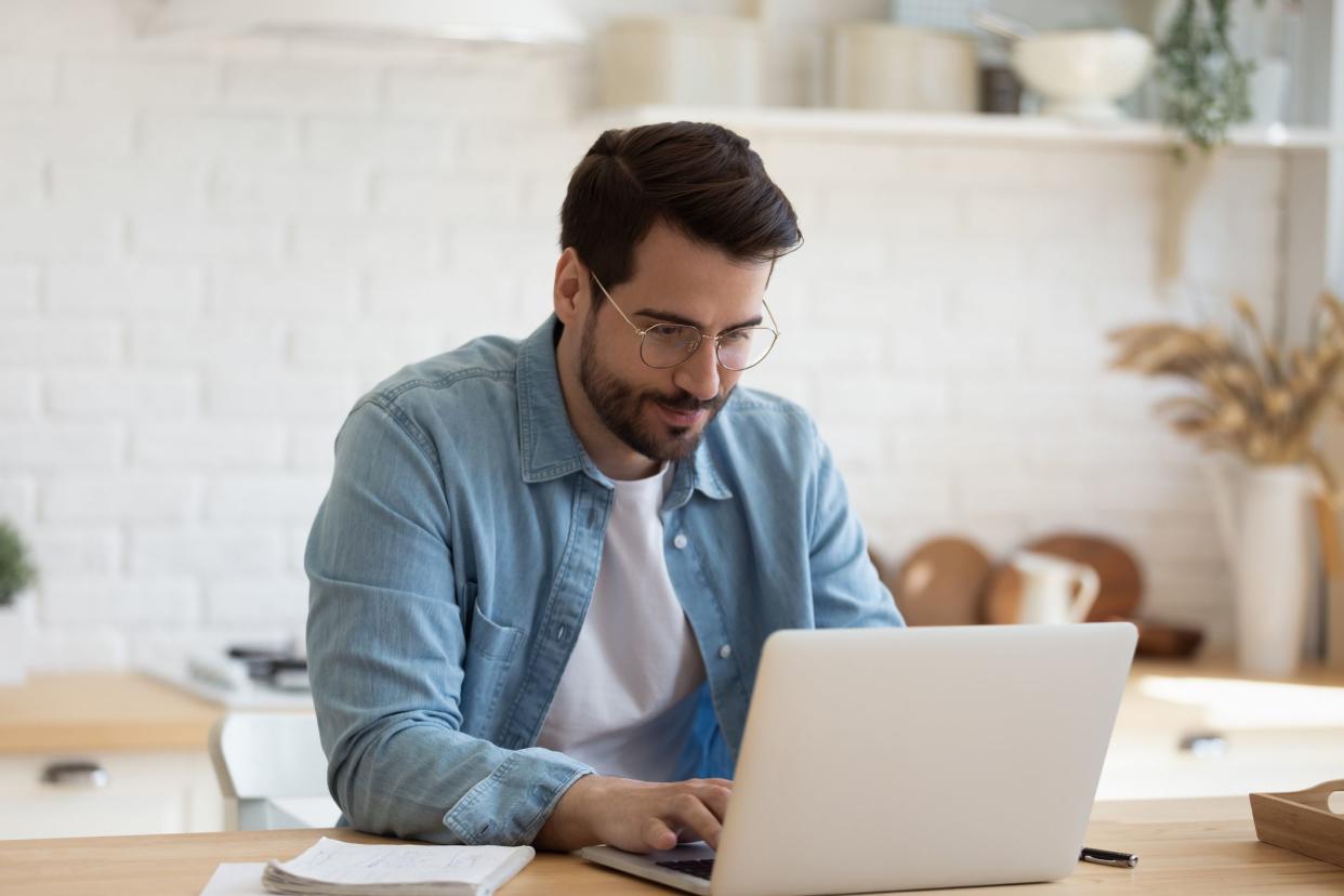 Head shot young businessman sitting at table with computer, working remotely, writing email or reading news. Young man attending distant educational courses, planning job or communicating online.