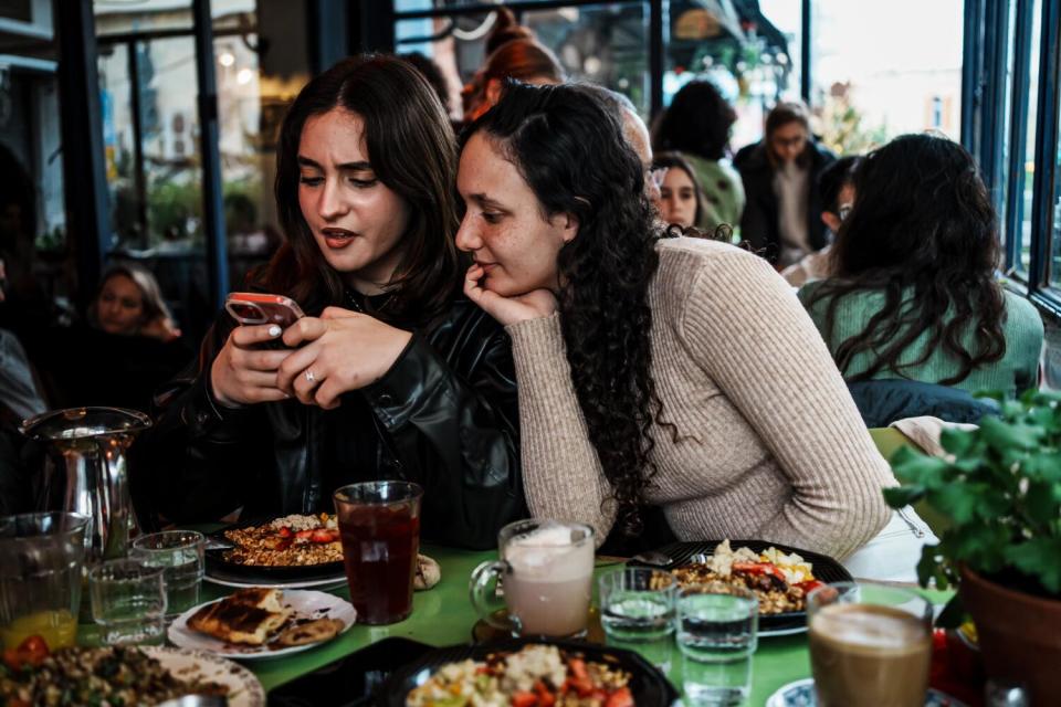 Angelina Shakkour and Adar Hirak look at pictures on Shakkour's cellphone at a restaurant