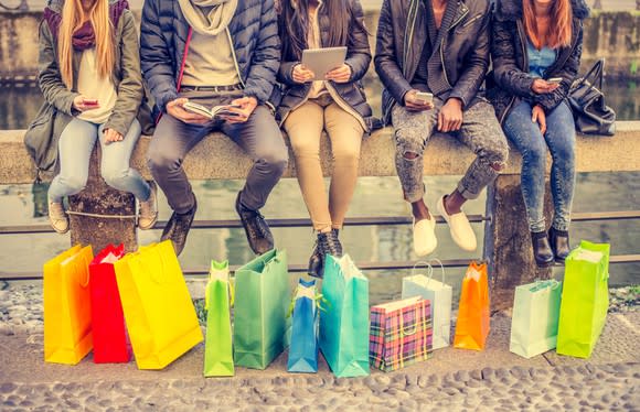 Five people sitting down after shopping, with shopping bags at their feet.