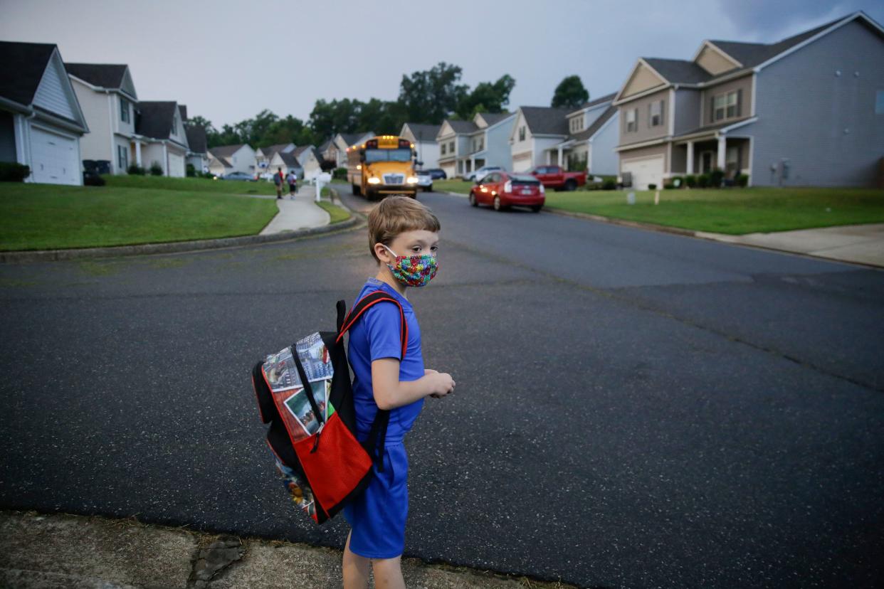 A 7-year-old boy wearing a mask waits at the bus stop on Aug. 3, the first day of school in Dallas, Georgia. (AP Photo/Brynn Anderson)