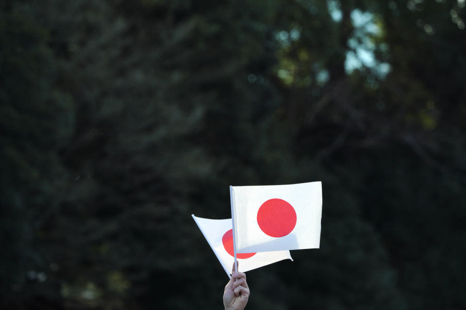 A visitor waves Japanese flags while waiting to see Japan's Emperor Naruhito's New Year public appearance with his imperial families at Imperial Palace in Tokyo Thursday, Jan. 2, 2020, in Tokyo. (AP Photo/Eugene Hoshiko)