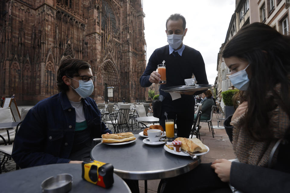 People enjoy a breakfast at a café terrace Wednesday, May, 19, 2021 outside the cathedral in Strasbourg, eastern France. Café and restaurant terraces are reopening Wednesday after a shutdown of more than six months deprived people of what feels like the essence of life — sipping coffee and wine with friends outdoors — to save lives during the coronavirus pandemic. (AP Photo/Jean-Francois Badias)