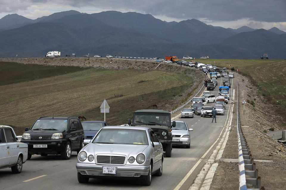 A convoy of several dozen cars on a stretch of road with mountains in the background.