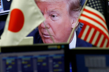 A TV monitor showing U.S. President Donald Trump is seen through national flags of the U.S. and Japan at a foreign exchange trading company in Tokyo, Japan February 1, 2017. REUTERS/Kim Kyung-Hoon