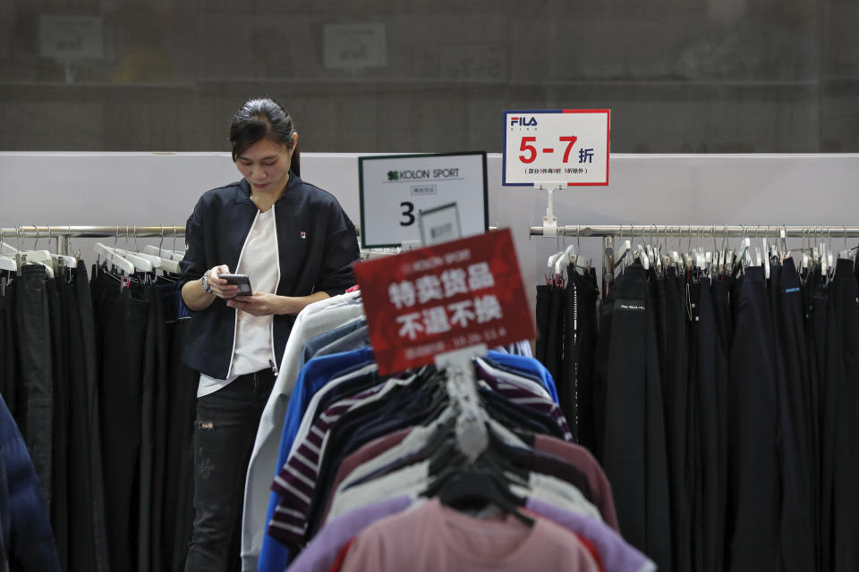 FILE - In this Nov. 1, 2019, file photo, an employee browses her smartphone at a clothing store having a promotion sale at a shopping mall in Shenzhen, China's Guangdong province. China has raised its estimate of the size of its economy by 2.1% following a census, raising its gross domestic product for 2018 to 91.93 trillion yuan ($13.1 trillion), the National Bureau of Statistics said Frida, Nov. 22, 2019. (AP Photo/Andy Wong, File)