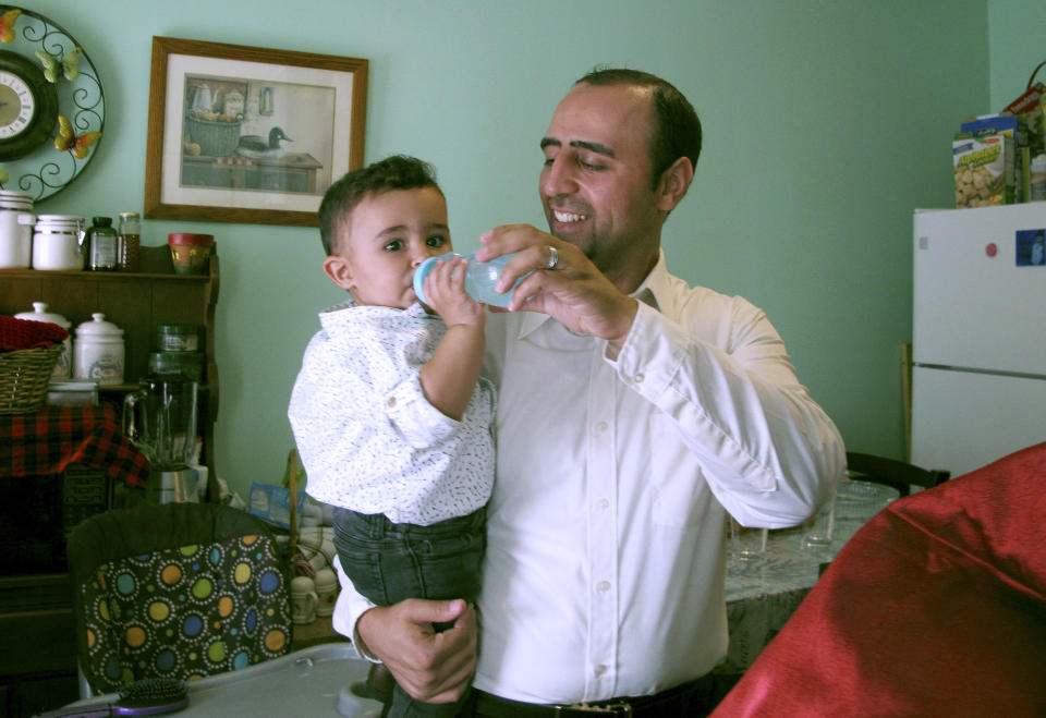 In this Aug. 5, 2019 photo, Hussam Alhallak holds a bottle for his son, Danyal, who was born in the United States, in the family's apartment in Rutland, Vt. Alhallak, his wife and their two older children fled the war in Syrian in 2015 and are rebuilding a life for themselves in Vermont. (AP Photo/Lisa Rathke)