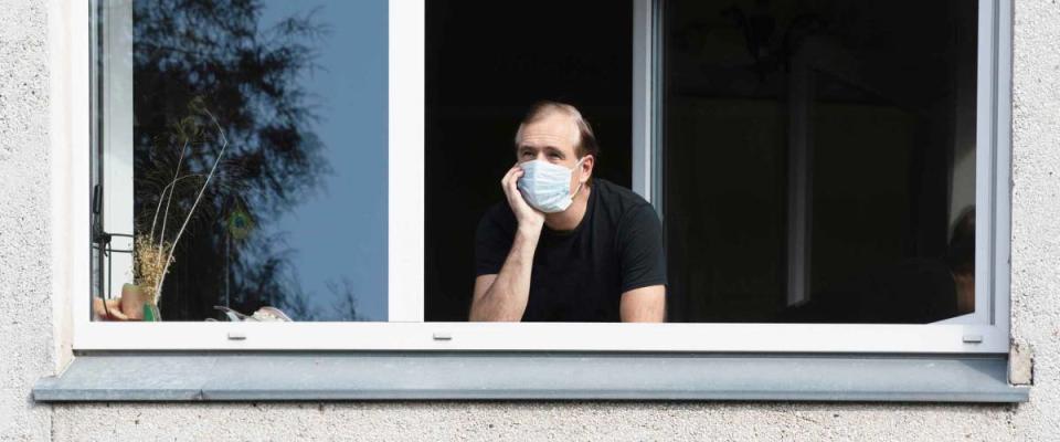 Man in medical face mask looking through window.