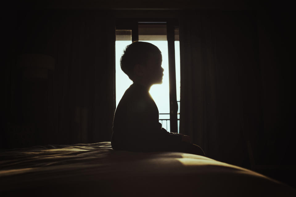 A boy sitting in a dark bedroom.