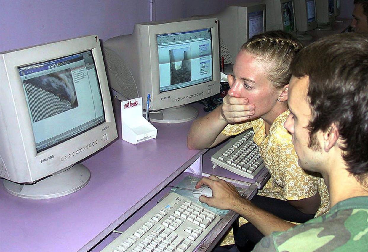 American tourists Ted Barnett (C) and Jamie Otten look at news photos of the attacks on the World Trade Centre buildings in a cybercafe in Calcutta, September 12, 2001. Three planes commandeered by hijackers slammed into the Pentagon and the twin towers of the World Trade Center yesterday.