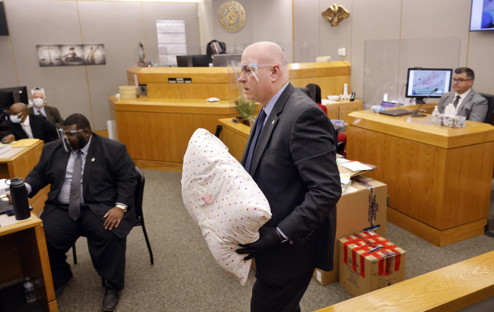 Prosecutor Glen Fitzmartin shows a lipstick stained pillow to the court after showing the evidence to Dallas Police detective Cayce Shelton, right, during the murder trial of Billy Chemirmir at the Frank Crowley Courts Building in Dallas, Tuesday, Nov. 16, 2021. Chemirmir faces life in prison without parole if convicted of capital murder in the death of 81-year-old Lu Thi Harris. (Tom Fox/The Dallas Morning News via AP, Pool)