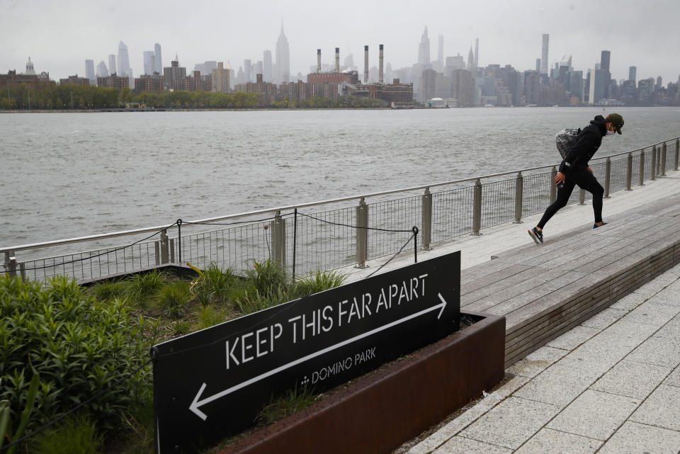 A visitor wearing a protective mask walks through Domino Park, Friday, May 8, 2020, in the Brooklyn borough of New York. Some parks will see stepped-up policing to stem the spread of the coronavirus, New York City Mayor Bill de Blasio said Friday. He also announced that 2,500 members of a "test and trace corps" will be in place by early June to combat the virus. (AP Photo/John Minchillo)