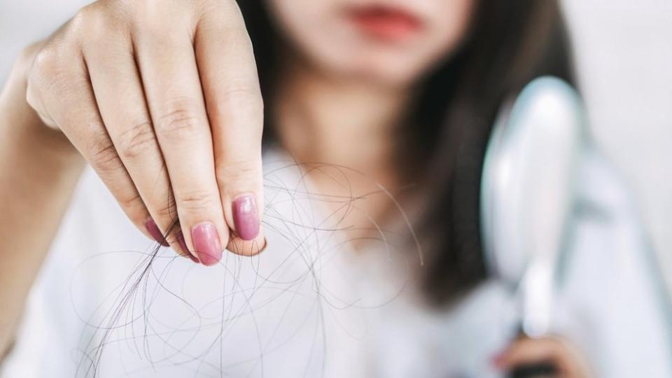 Una mujer sosteniendo unos cabellos en la mano.