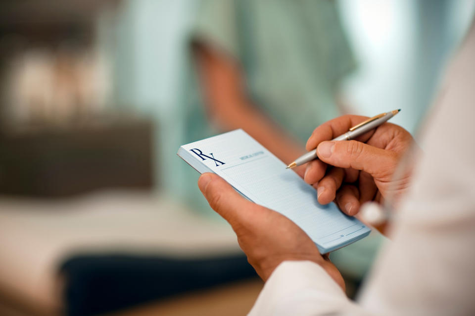 A doctor holding a prescription pad writes with a pen, with a patient blurred in the background