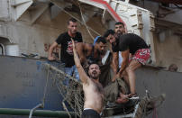 Civilians help to evacuate an injured sailor from a ship which was docked near the explosion scene that hit the seaport of Beirut, Lebanon, Tuesday, Aug. 4, 2020. (AP Photo/Hussein Malla)