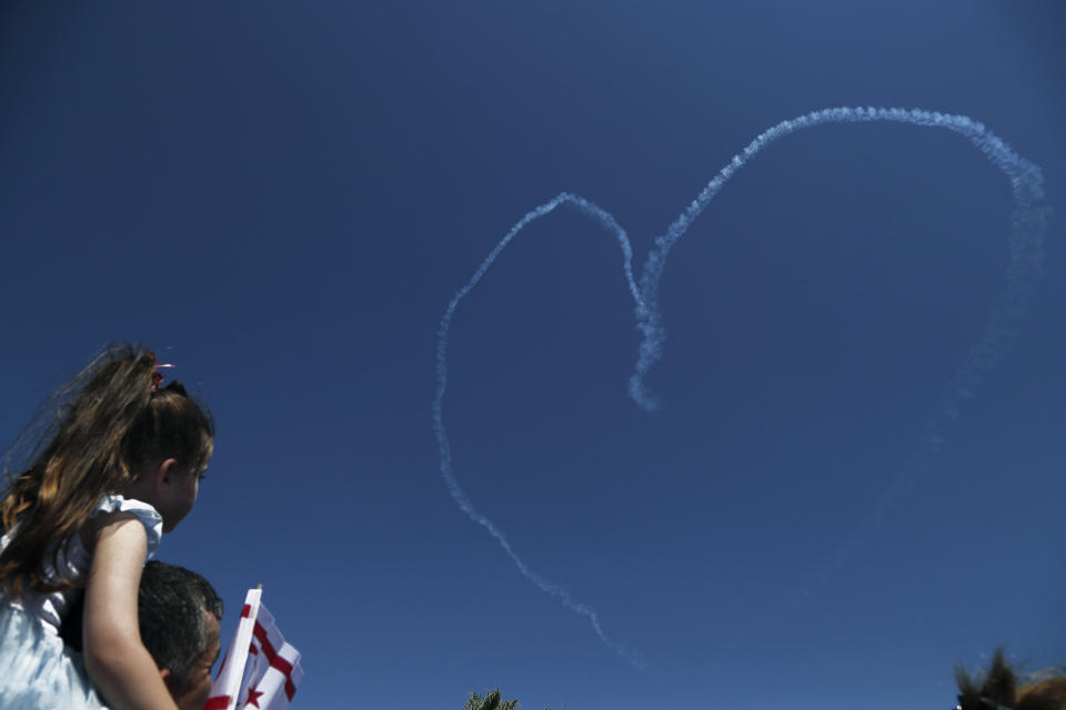 A girl sits on her father's shoulders as they watch the Turkish acrobatic aircraft jets make a heart sign in the sky, during a military parade celebration marking the 45th anniversary of the 1974 Turkish invasion in the Turkish occupied area of the divided capital Nicosia, Cyprus, Saturday, July 20, 2019. Cyprus was split into Greek Cypriot south and Turkish Cypriot north in 1974 when Turkey invaded in response to a coup by supporters of union with Greece. (AP Photo/Petros Karadjias)