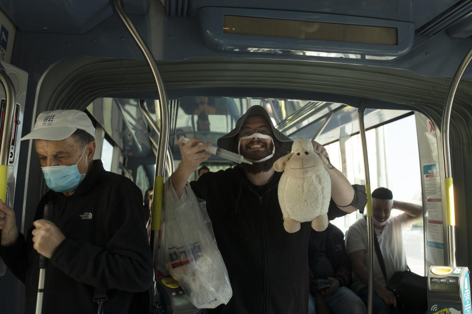 A man who opposes coronavirus vaccine mandates wears a mask altered to make a statement, poses with a toy sheep and an outsized syringe as he rides a crowded train in Jerusalem ahead of Shabbat, Friday, Nov. 26, 2021. Israel's prime minister says it is "on the threshold of an emergency situation" after authorities detected the country's first case of a new coronavirus variant in a traveler who returned from Malawi. (AP Photo/Maya Alleruzzo)