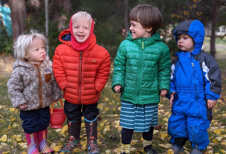 four kids ages 2-4 in snowsuits, jackets, fleeces, and layers, they are all smiling