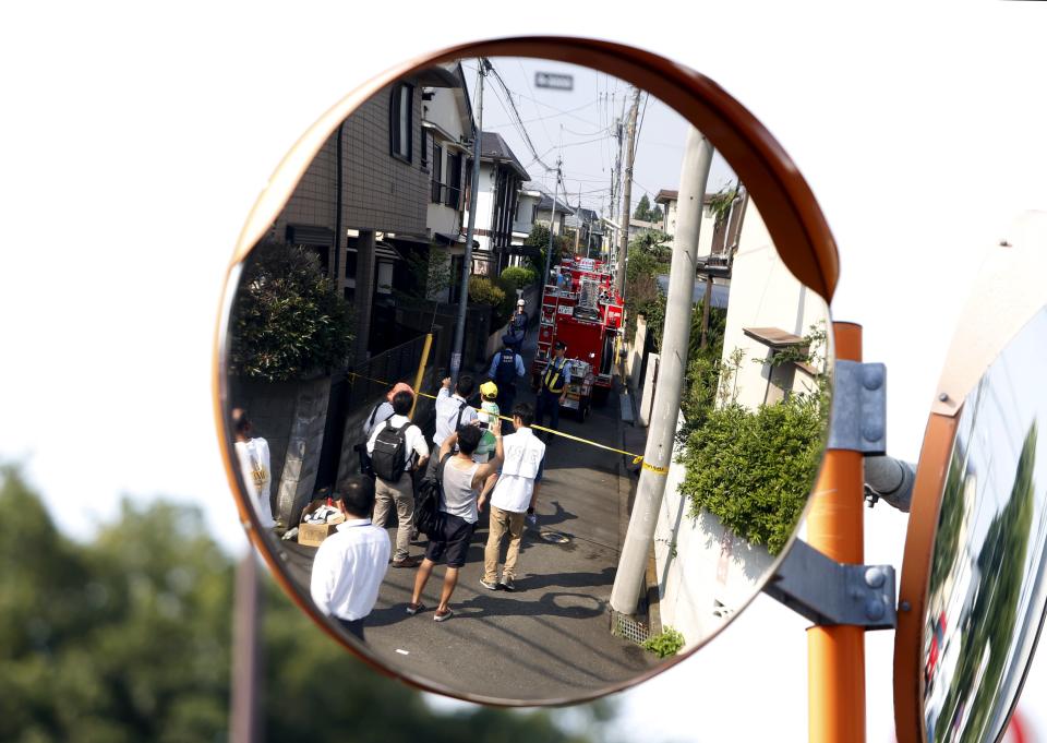 A reflection of onlookers are seen from a traffic mirror along a street in front of the site where a light plane went down in a residential area and burst into flames, in Chofu, outskirt of Tokyo, July 26, 2015. (REUTERS/Yuya Shino)