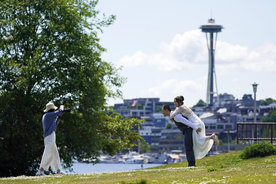 FILE- In this May 10, 2021 file photo, Tom Li, second from right, and his fiancé, Leah Li, right, pose for photos taken by Ella Chang, left, at Gas Works Park in Seattle. The couple, who live in Seattle, are originally from China and have a wedding planned later in the year for September. As COVID-19 cases drop and restrictions ease, many couples are eagerly moving forward with paused wedding plans — or altering existing ones to accommodate more guests. But figuring out where to start and what costs you’ll face can still be tricky during this time. (AP Photo/Ted S. Warren, File)