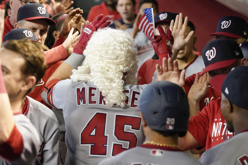 Wearing a wig and waving a United States flag, Washington Nationals' Joey Meneses is greeted by teammates after hitting a three-run home run against the Arizona Diamondbacks in the ninth inning during a baseball game, Sunday, May 7, 2023, in Phoenix. (AP Photo/Darryl Webb)