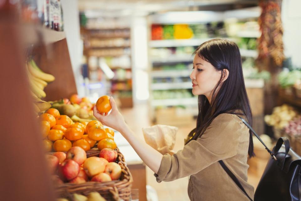 A woman picks up an orange in a grocery store