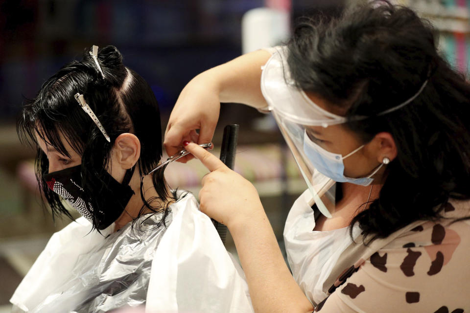 Stylist Hayley Hehir, right, cuts the hair of client Francesca Shashkova at Tusk Hair in Camden, London, after opening at midnight to the first post-lockdown customer as restrictions are eased across England early Saturday, July 4, 2020. The easing of restrictions, which were imposed on March 23, allows businesses including pubs, restaurants and hair salons, to reopen to members of the public with measures in place to prevent the spread of the coronavirus. (Jonathan Brady/PA via AP)