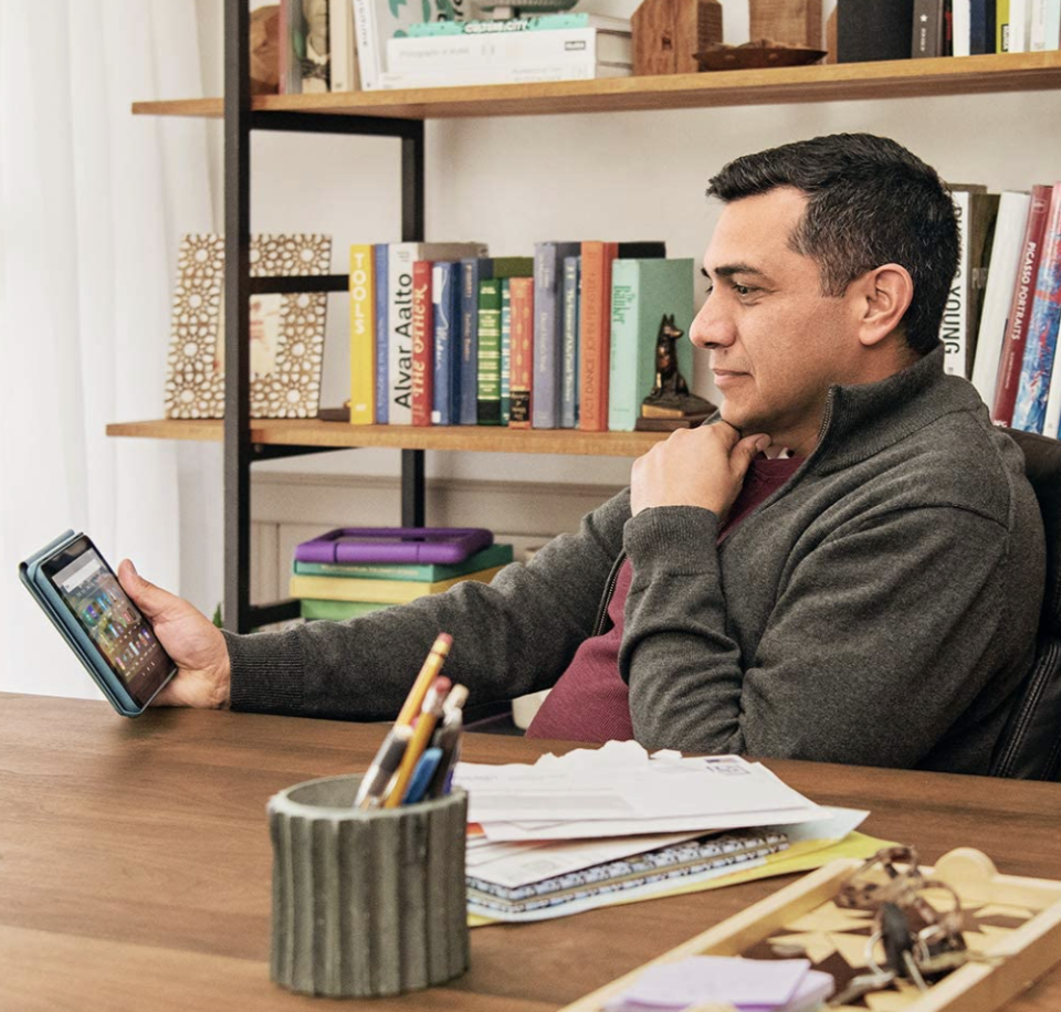 man sitting in front of book case holding amazon Fire HD 8 tablet (Photo via Amazon)