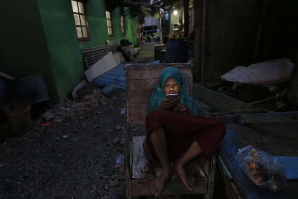 In this Tuesday. Oct. 15, 2019, photo, a girl checks her mobile phone at a slum in Jakarta, Indonesia. Known for his down-to-earth style with a reputation for clean governance, Indonesian President Joko Widodo's signature policy has been improving Indonesia's inadequate infrastructure and reducing poverty, which afflicts close to a tenth of Indonesia's nearly 270 million people. But raising money would be harder at a time of global economic slowdown, major trade conflicts and falling exports. (AP Photo/Tatan Syuflana)